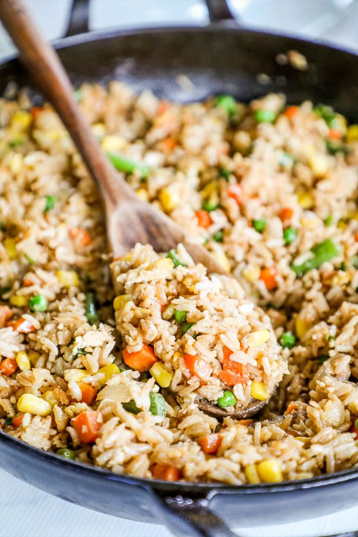 rice and vegetables being cooked in a skillet with a wooden spoon on the side