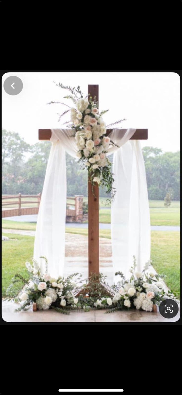 a cross decorated with white flowers and greenery for a wedding in the country side