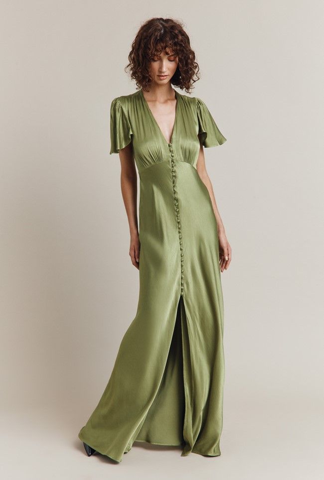 a woman in a long green dress with buttons on the front and side, standing against a