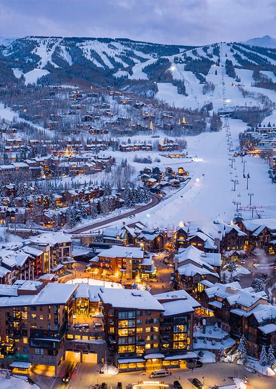 an aerial view of a ski resort and surrounding buildings at night time with snow on the ground