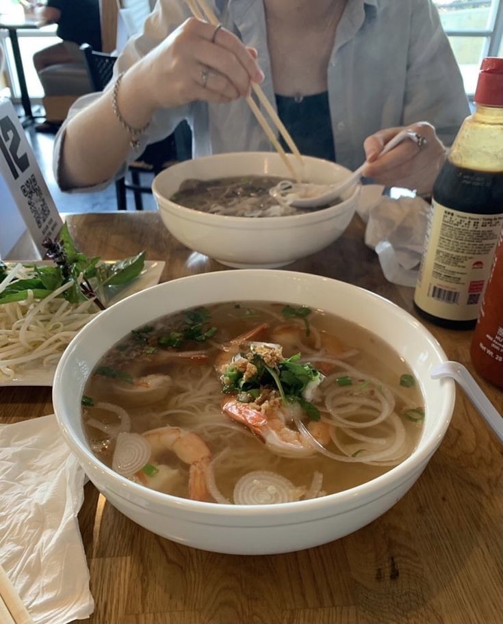 a woman sitting at a table with a bowl of soup and chopsticks