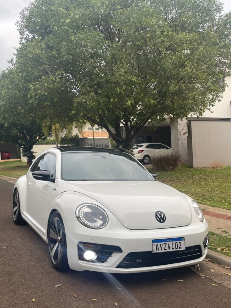 a white volkswagen beetle parked on the side of the road in front of a house