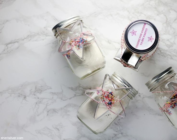 three glass jars filled with confetti and sprinkles on a marble surface