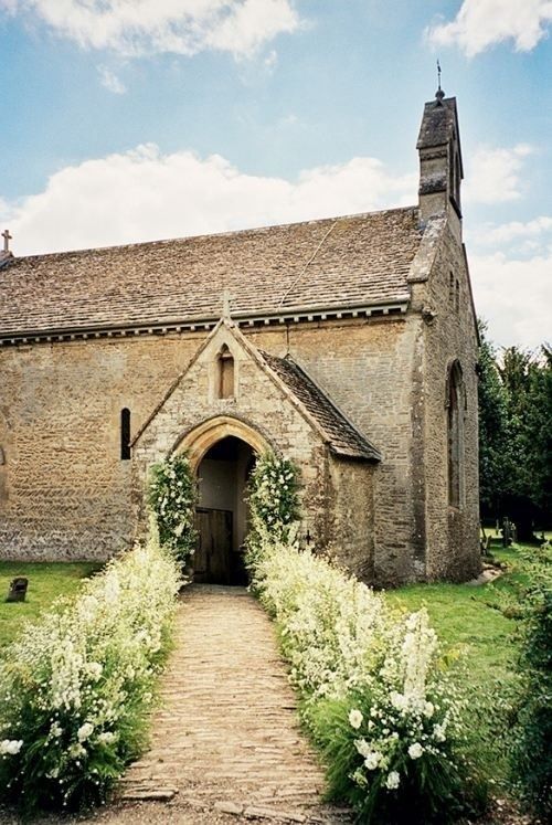 an old stone building with white flowers growing on the front door and walkway leading up to it