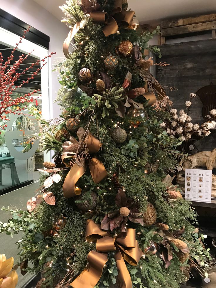 a christmas tree decorated with gold and green ribbons, pine cones, ornaments and greenery