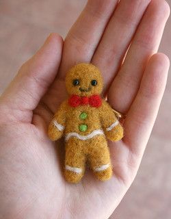 a hand holding a tiny teddy bear wearing a red bow tie and green buttons on it's chest