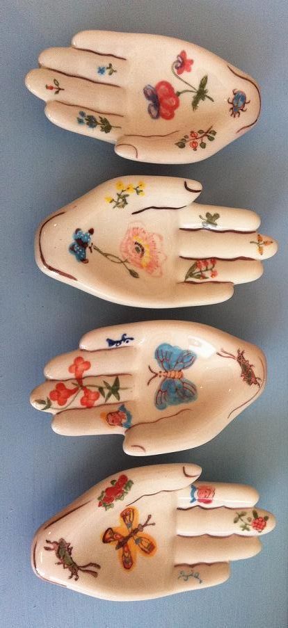 three hand - shaped dishes with flowers and butterflies painted on them are lined up against a blue wall