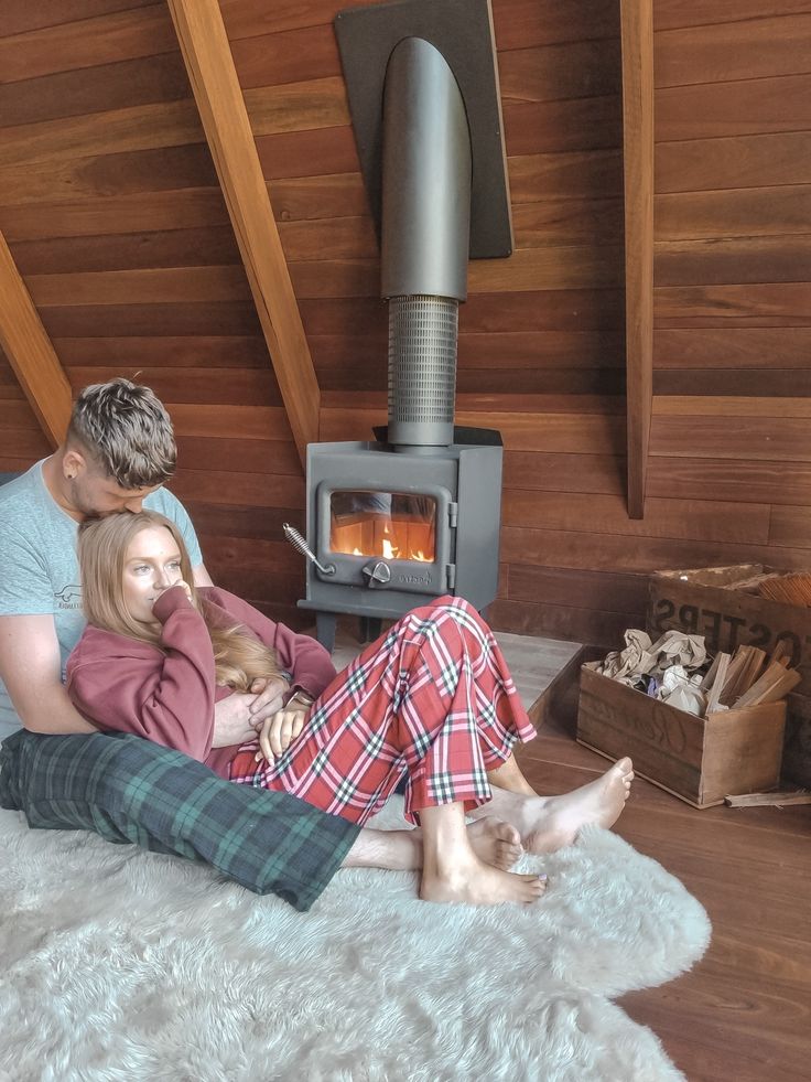 a man and woman sitting on the floor in front of an open fire place with logs