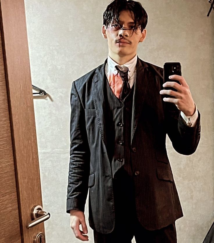 a man in a suit taking a selfie with his cell phone while standing in front of a door