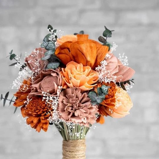 an orange and pink bouquet in a vase on a table with grey brick wall behind it