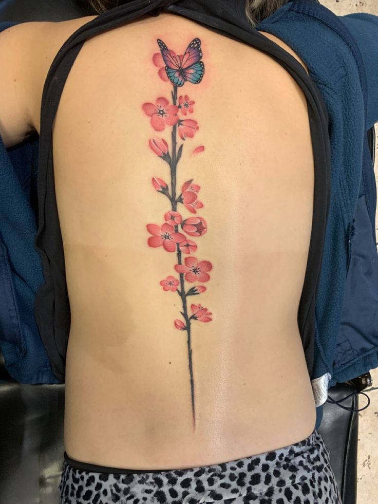 the back of a woman's body with flowers and a butterfly tattoo on it