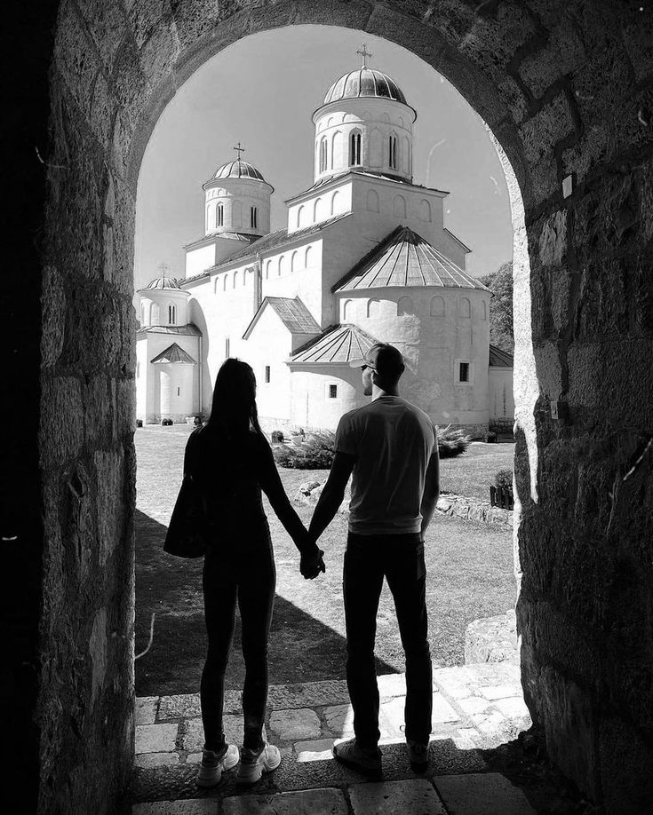 a man and woman hold hands as they walk through an archway in front of a church