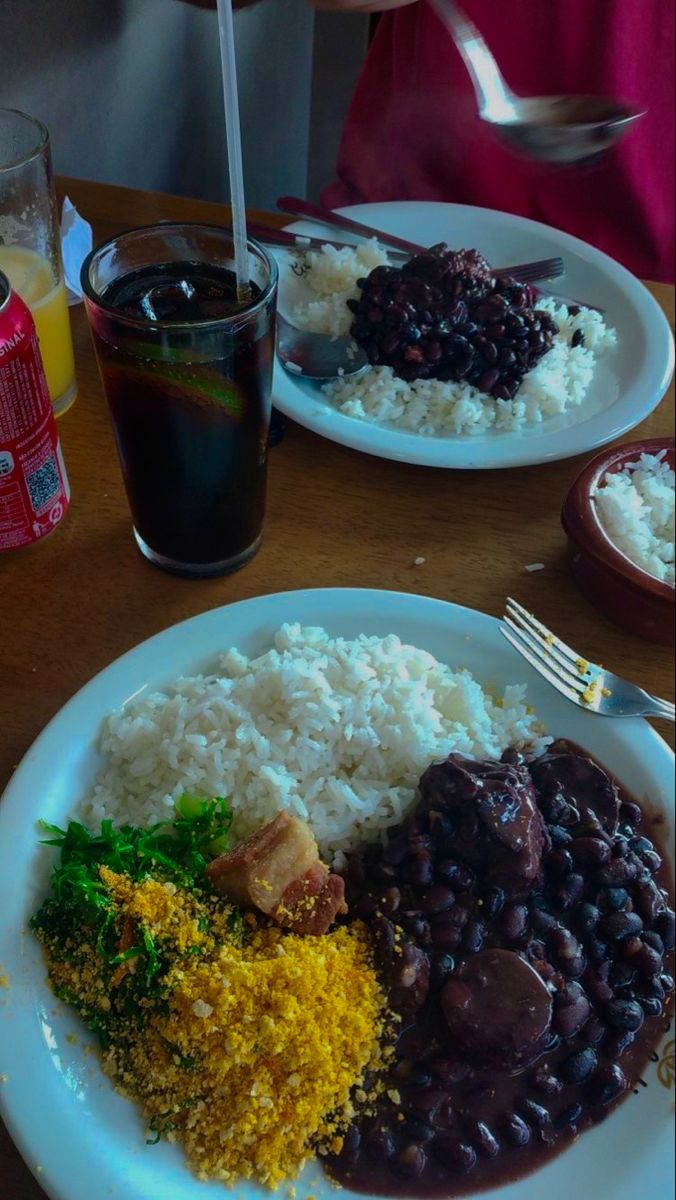 two white plates filled with rice, beans and other food on top of a wooden table