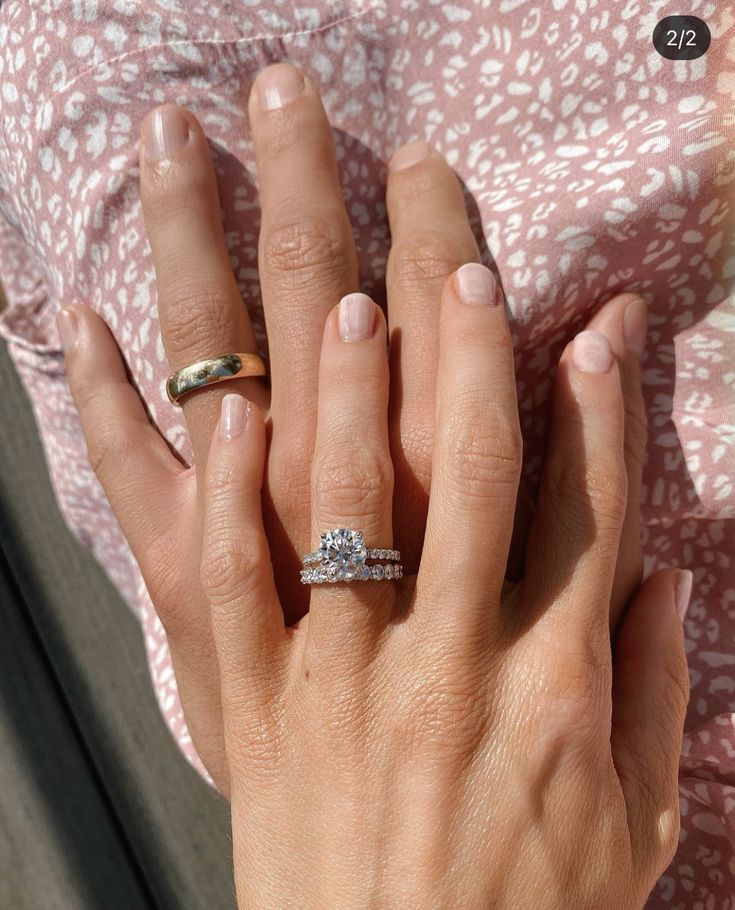 a woman's hand with two engagement rings on her left and the other hand holding an engagement ring