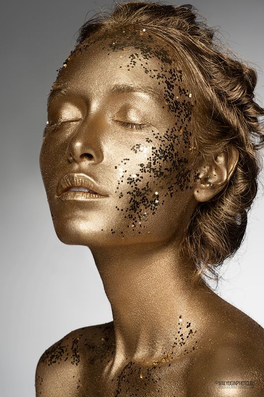 a woman with gold glitter on her face and chest, she is looking to the side