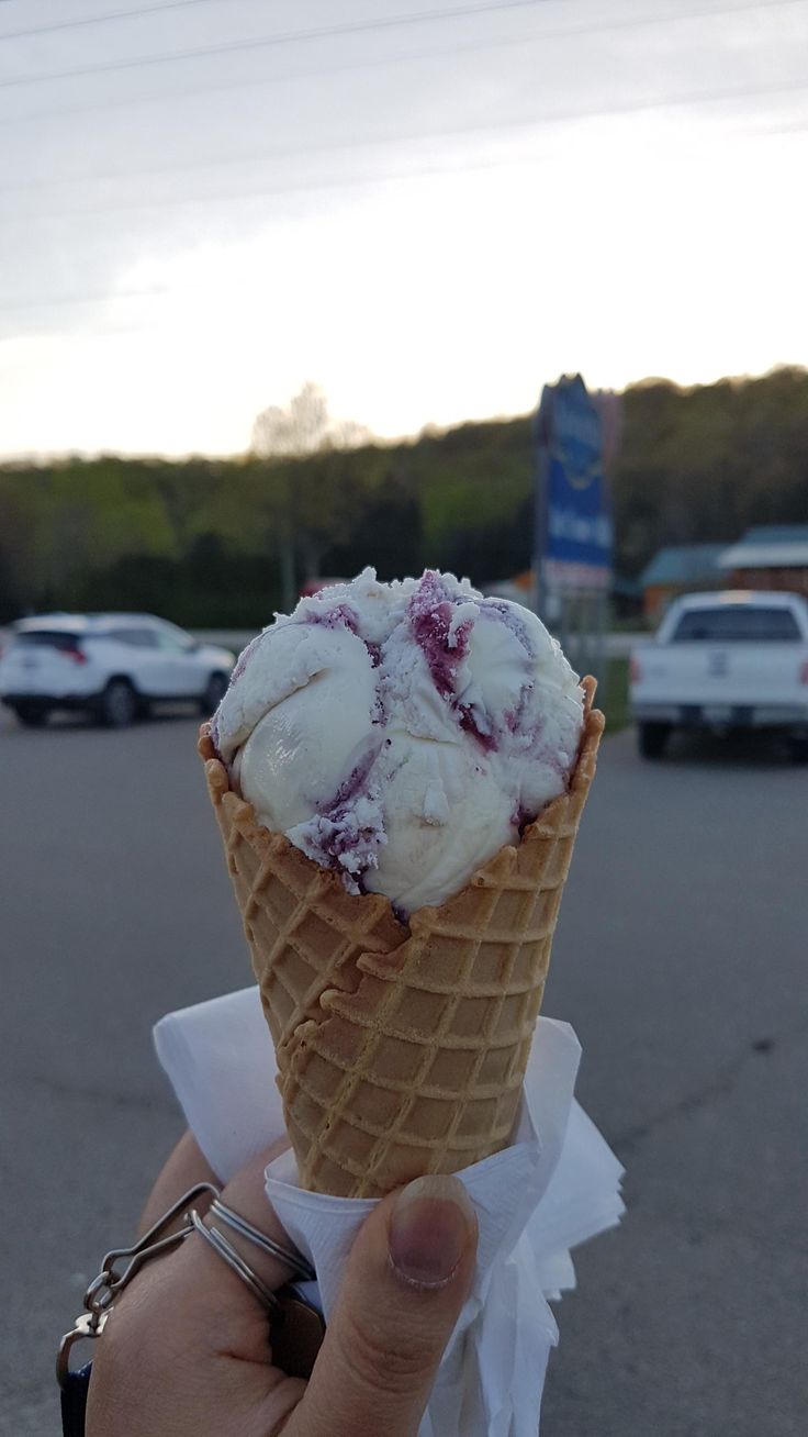 someone holding up an ice cream cone with cranberry sauce on it in a parking lot