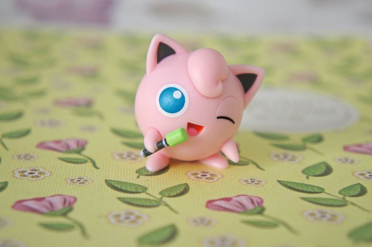 a small pink toy pig sitting on top of a green tablecloth covered with flowers