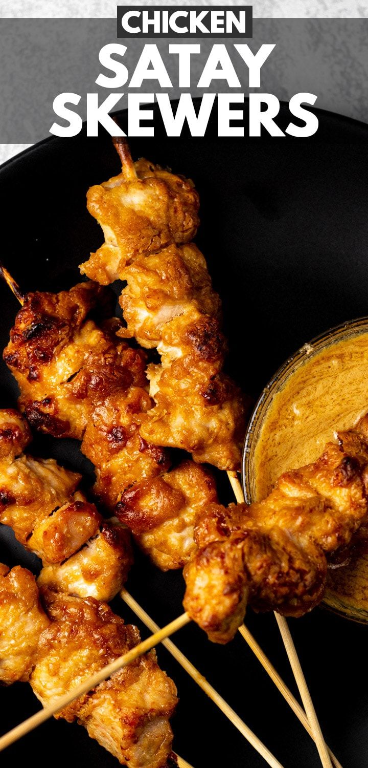 chicken satay skewers on a black plate with dipping sauce in the background