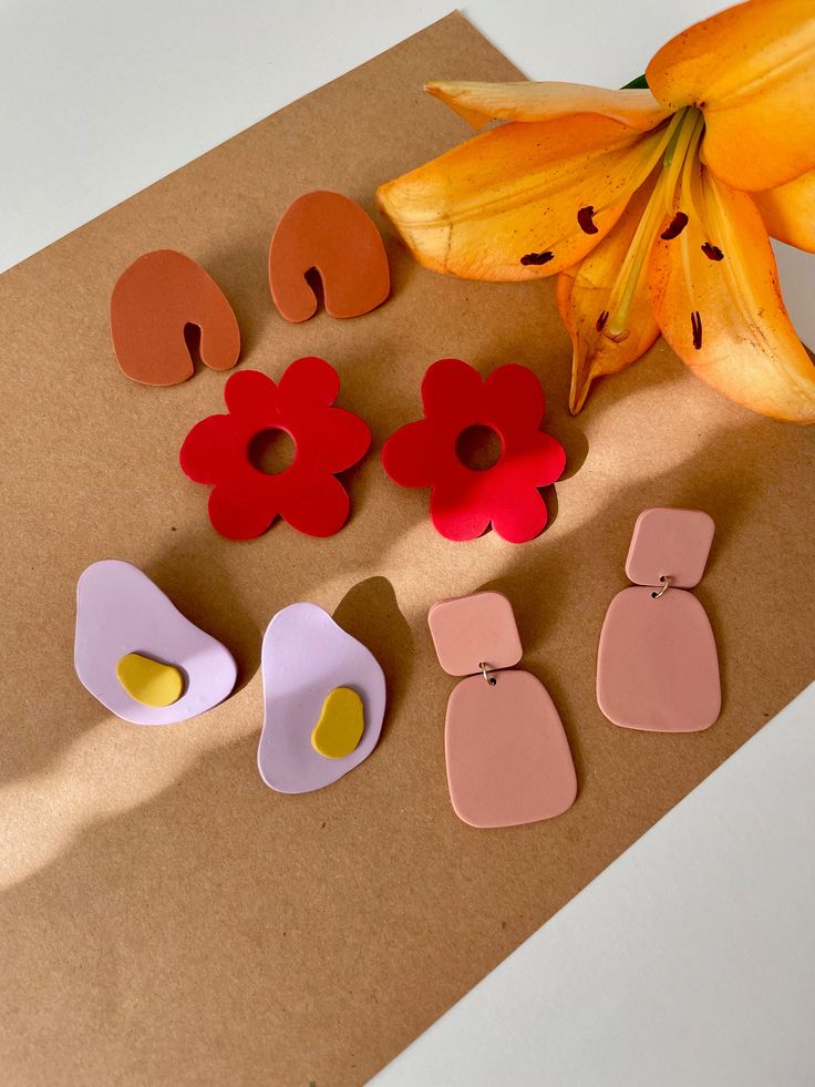 three pairs of earrings sitting on top of a piece of paper next to a flower