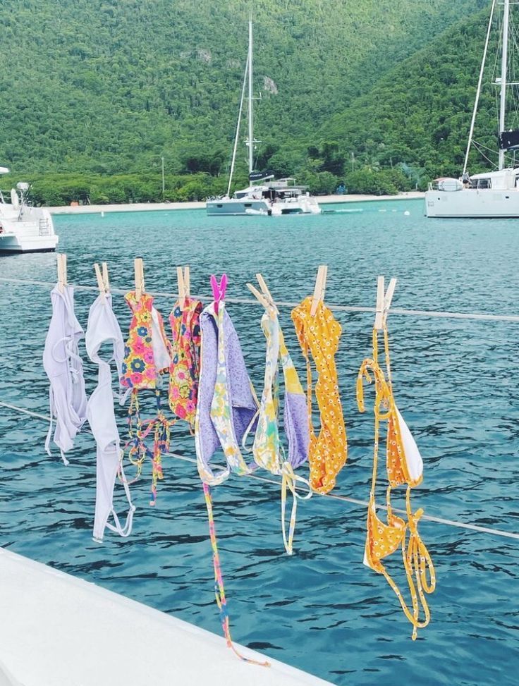 several colorful ties hanging on a clothes line near the water with boats in the background