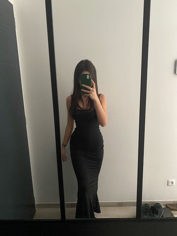 a woman in a black dress taking a selfie with her cell phone while standing in front of a mirror