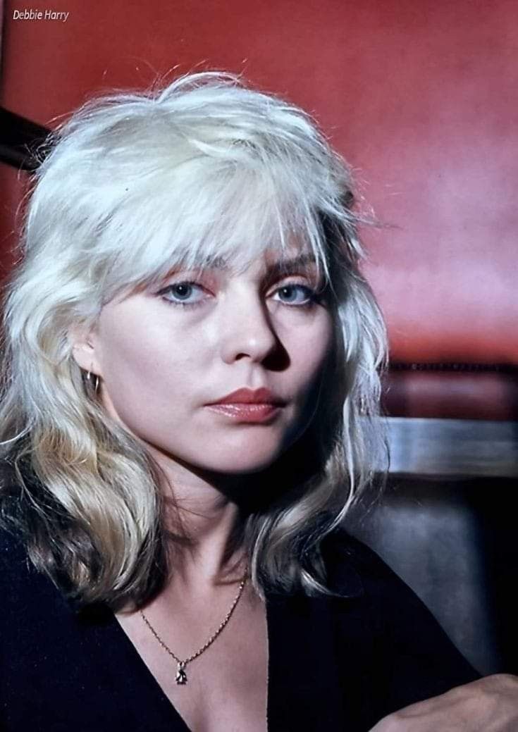 a woman with blonde hair and blue eyes sitting in a chair looking at the camera