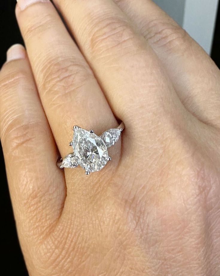 a woman's hand holding an engagement ring with two pear shaped diamonds on it