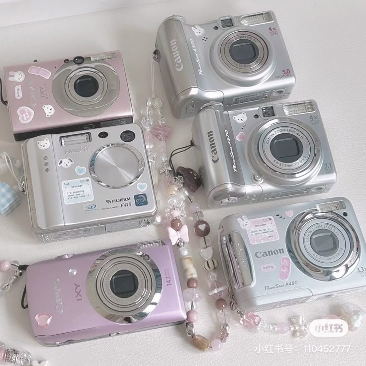 four cameras sitting next to each other on top of a white surface with beads around them