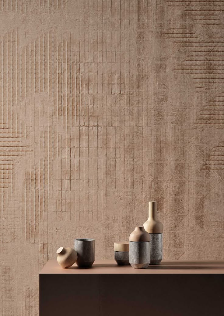 three vases sitting on top of a wooden table next to a wall with a textured background