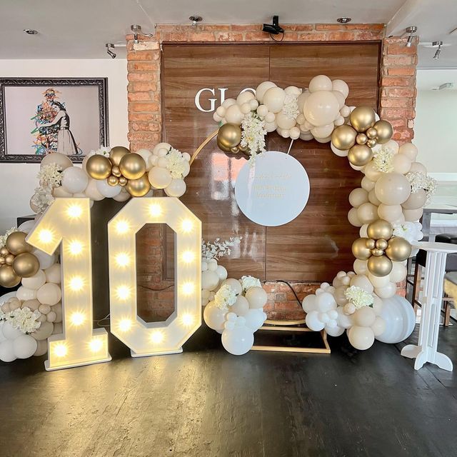 a large balloon arch with the number 10 surrounded by white and gold balloons in front of a brick wall