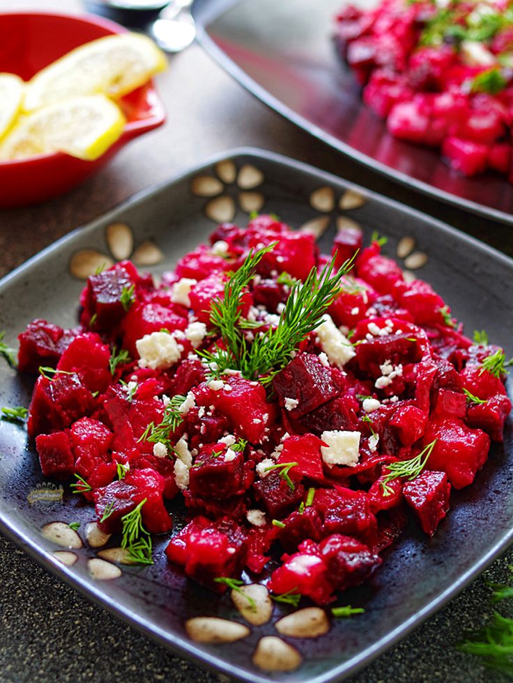 two plates with beets and cheese on them next to some lemon wedges,