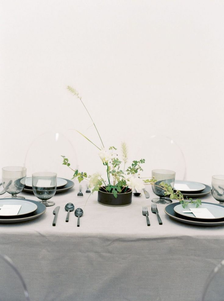 the table is set with plates, silverware and greenery in a bowl on it