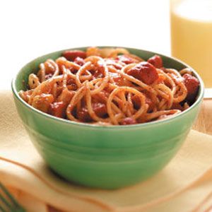 a green bowl filled with spaghetti next to a glass of orange juice