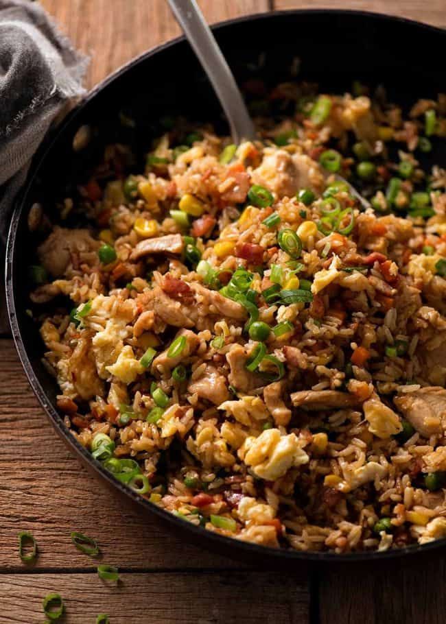 a skillet filled with rice and vegetables on top of a wooden table next to a napkin