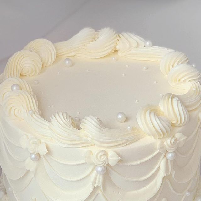 a close up of a white frosted cake with icing swirls and pearls