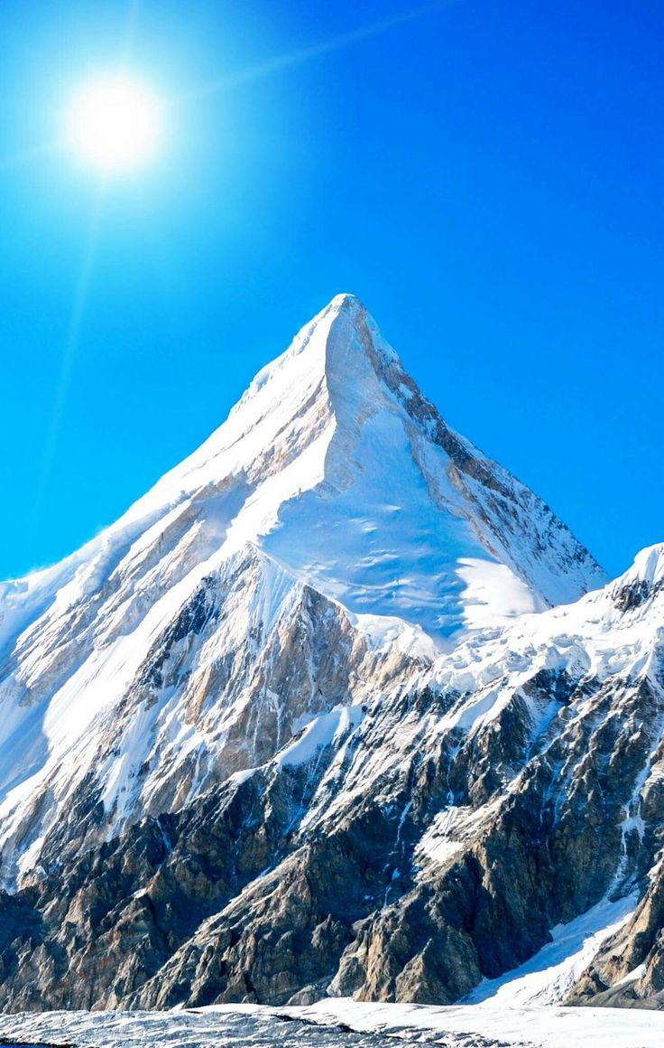 a snow covered mountain with the sun shining on it's top and blue sky