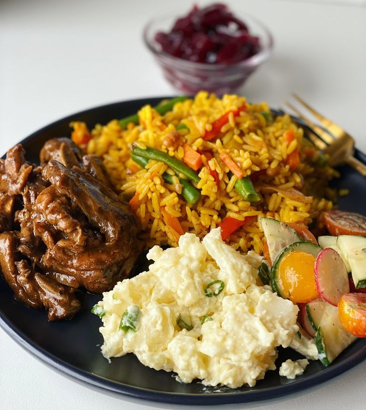 a black plate topped with rice, meat and veggies next to other foods