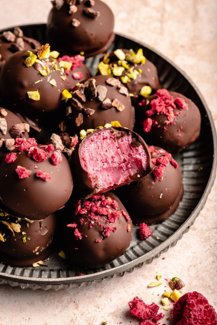 a plate full of chocolate truffles with raspberries and pistachio sprinkles