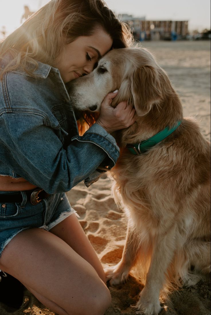 a woman sitting on the beach with her dog and kissing her face in front of her