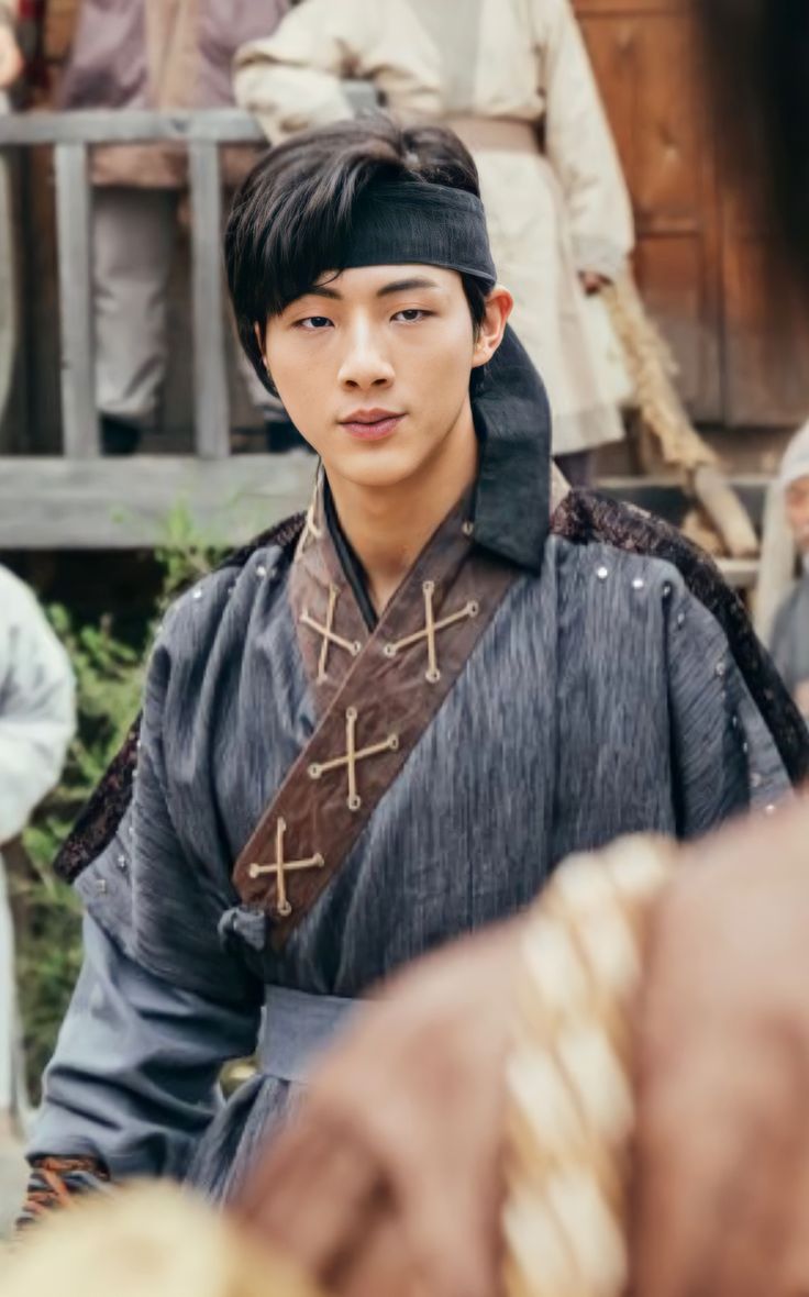 a young man dressed in medieval clothing standing next to other people and looking at the camera