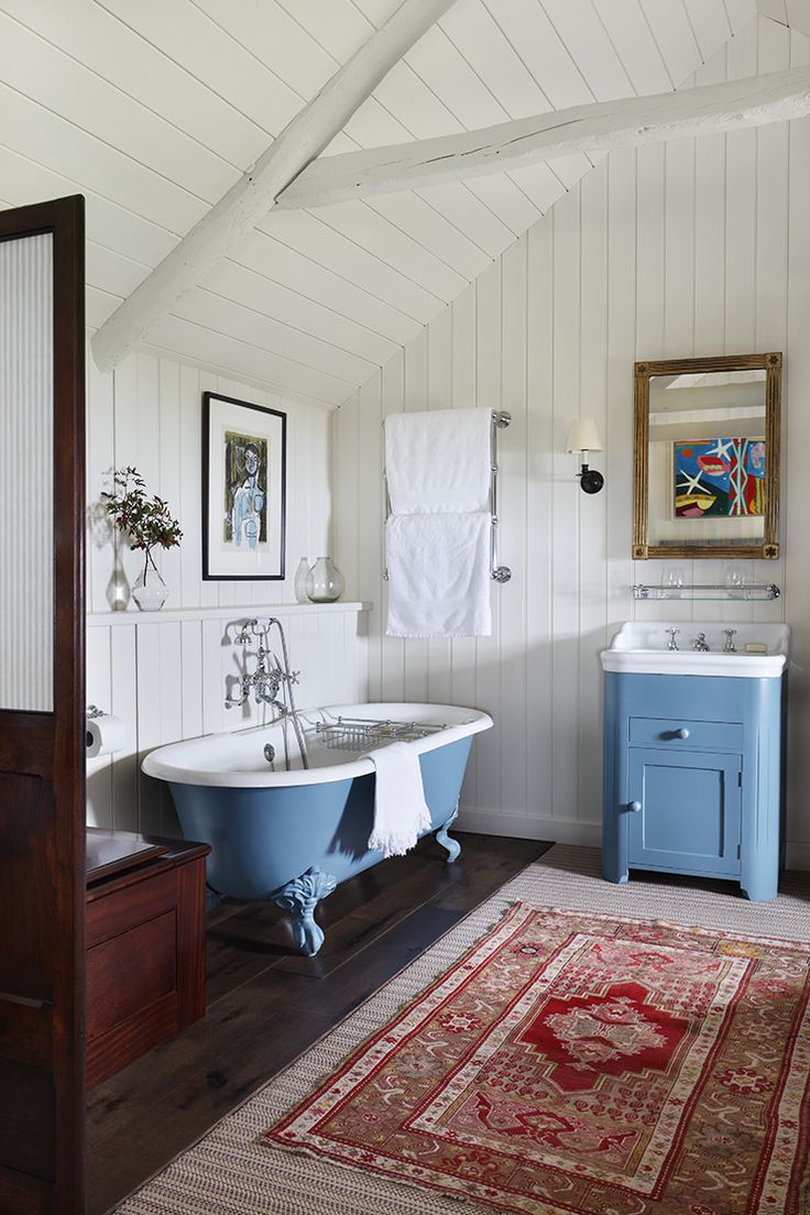 an old fashioned bathtub and rug in a bathroom with white walls, wood floors and ceiling