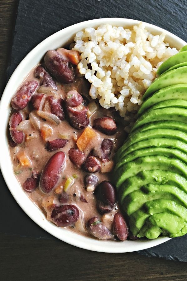 a bowl filled with beans, rice and avocado on top of a table