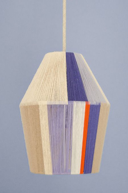 a multicolored lamp hanging from a string on a blue wall with an orange, purple, and white striped light fixture