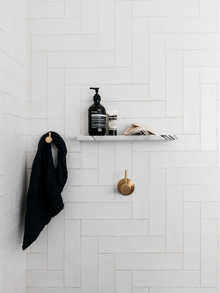 a bathroom with white tile and gold accessories on the shelf, along with a black towel