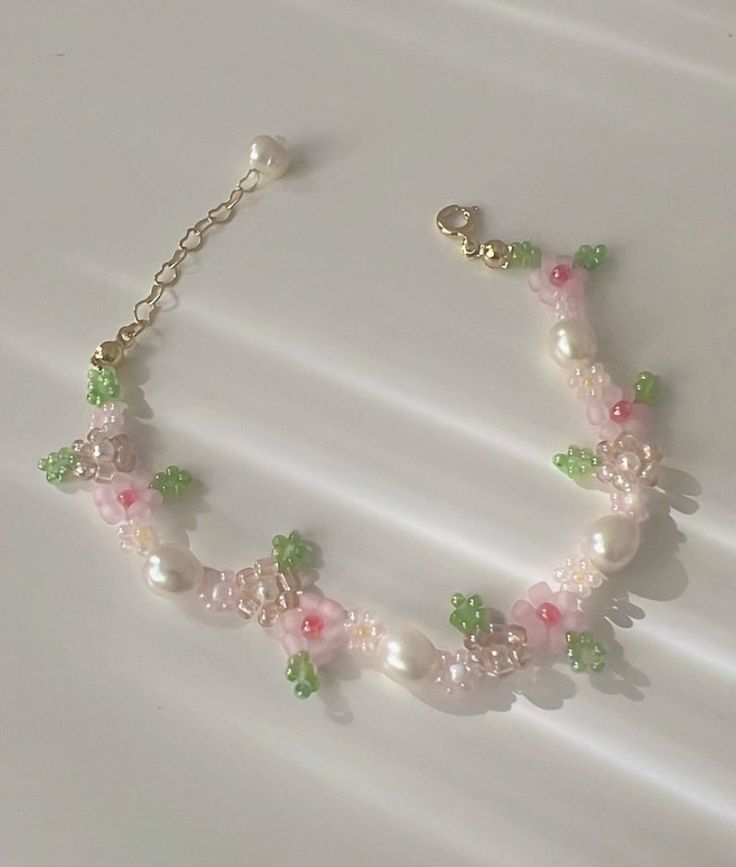 a pink and green beaded bracelet on a white surface with pearls, flowers and leaves