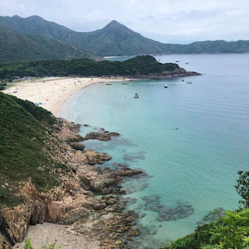 an aerial view of a beach with boats on the water and mountains in the background