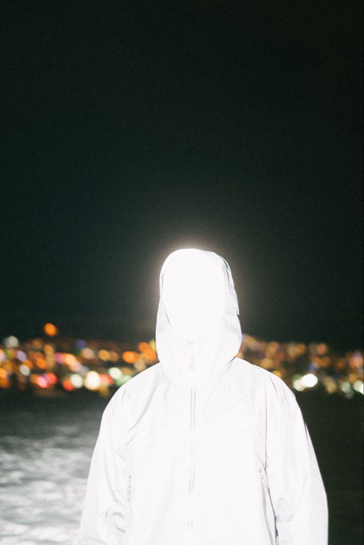 a person standing in the water at night wearing a white raincoat and hoodie