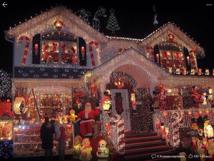 a house covered in christmas lights and decorations with people standing outside the front door looking at it