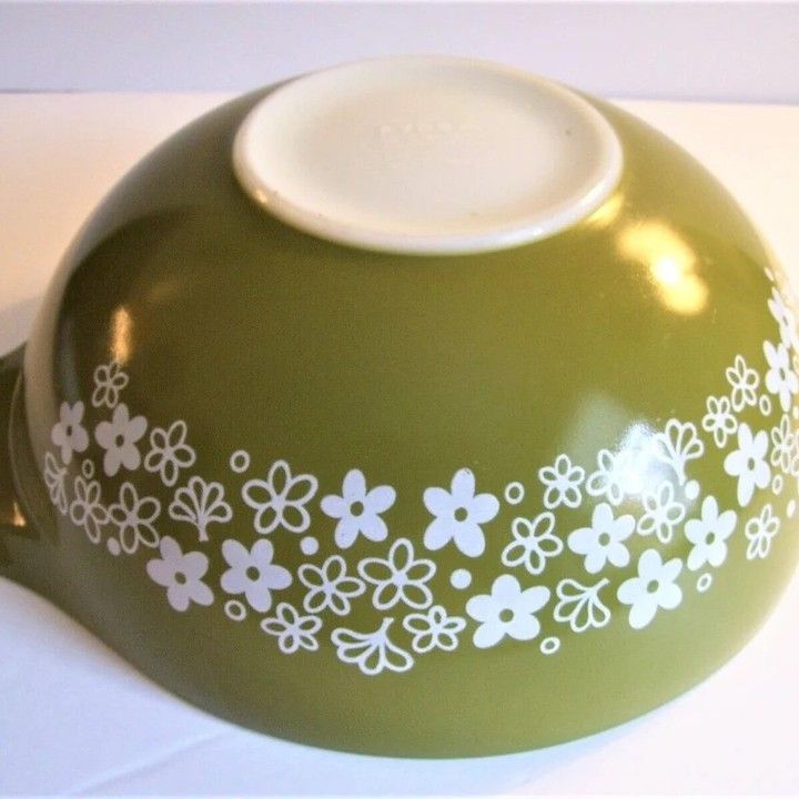 a green vase with white flowers painted on the side and bottom, sitting on a table