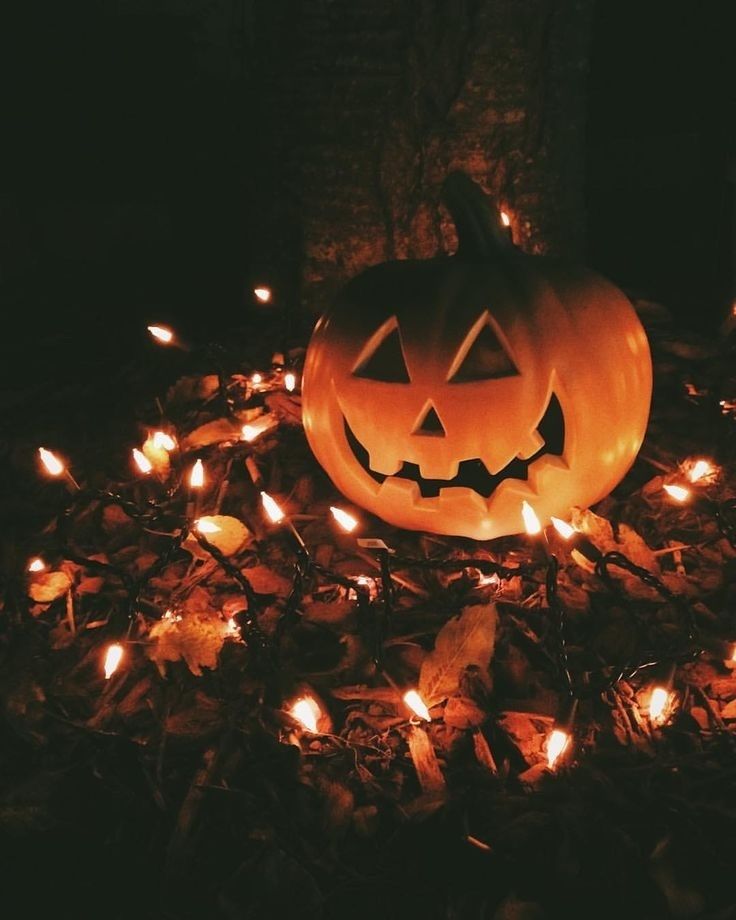 a halloween pumpkin sitting in the middle of a pile of leaves with words happy halloween on it